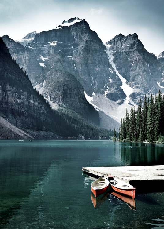  – Fotografie eines Sees mit einem kleinen Steg und zwei Kanus vor Bergen