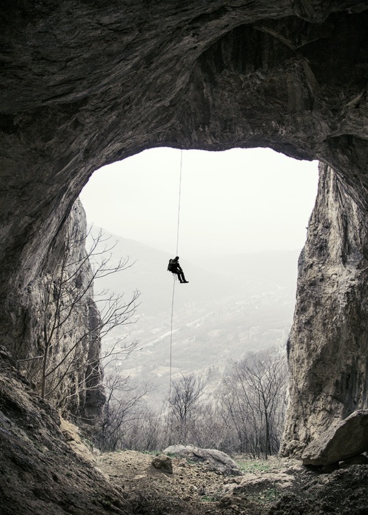  - Schönes Foto, das aus einer Berghöhle heraus einen sich abseilenden Bergsteiger zeigt.