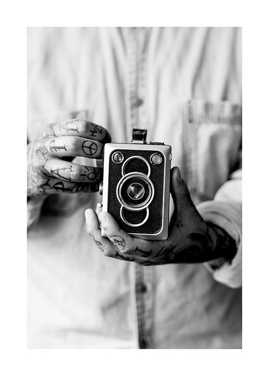  – Schwarz-weiß-Fotografie, die eine Vintage-Kamera in den Händen eines Mannes mit tätowierten Händen zeigt
