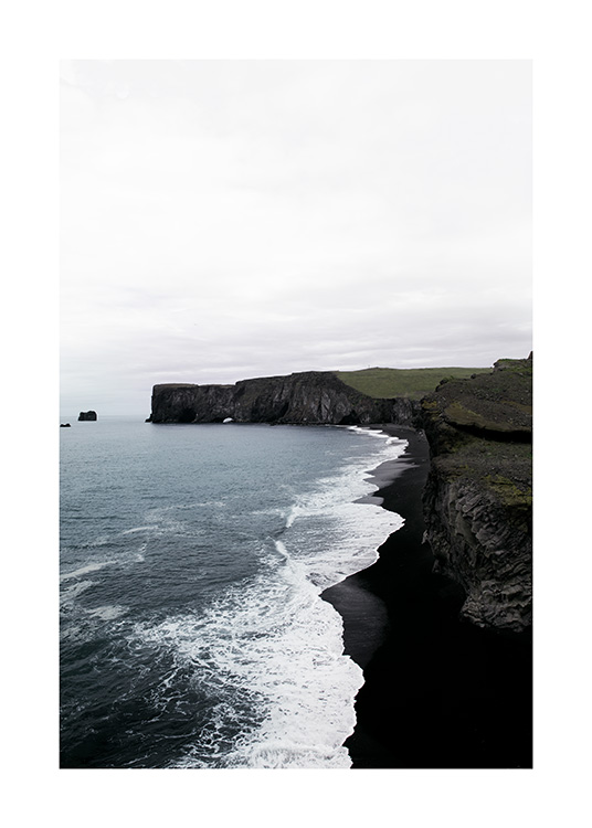  - Fotografie einer Küstenlinie mit schwarzen Felsen, einem schwarzen Strand und Meeresbrandung
