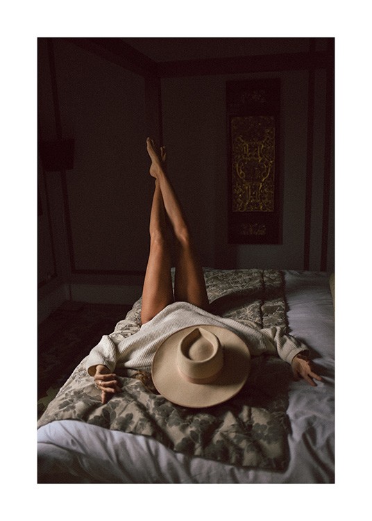  – Fotografie einer Frau, die auf einem Bett liegt, die Beine in die Luft gestreckt und ihr Gesicht durch einen Hut bedeckt