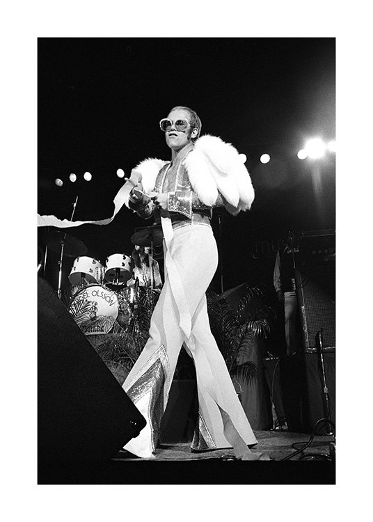  – Schwarz-weiß-Fotografie des Sängers Elton John, der einen weißen Overall und eine Sonnenbrille auf der Bühne trägt