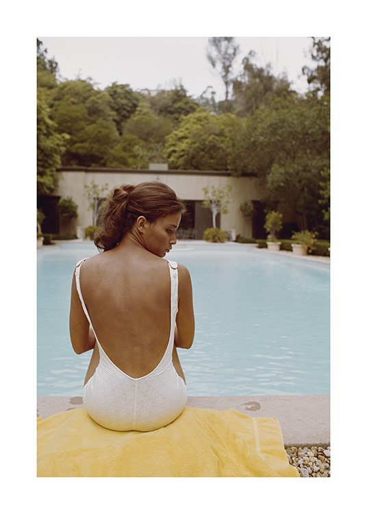  – Fotografie einer Frau in weißem Badeanzug, die auf einem Handtuch vor einem Pool sitzt