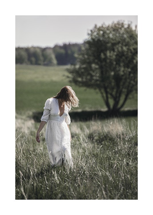  – Fotografie einer Frau, die in einem weißen, langen Kleid in hohem Gras steht, im Hintergrund Bäume