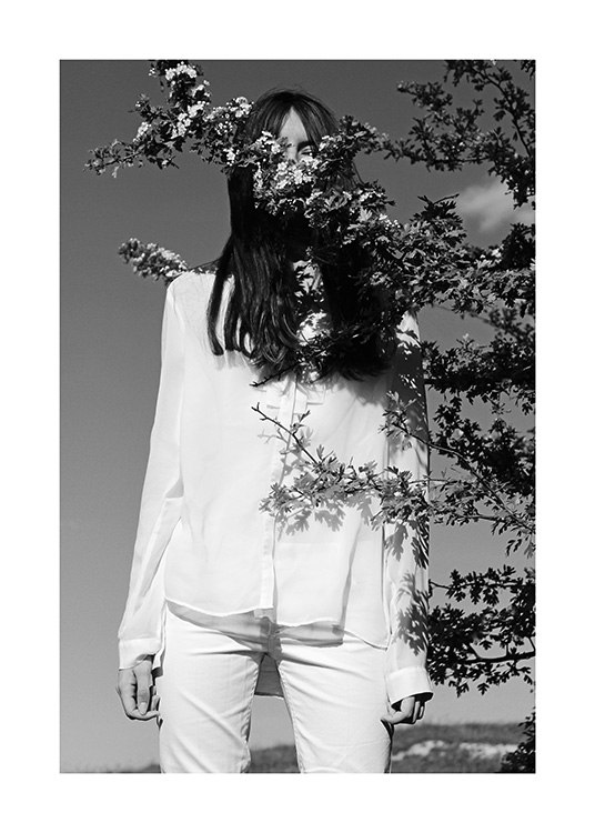  – Schwarz-weiß-Fotografie einer Frau in weißer Kleidung, vor ihr der Zweig eines Baumes