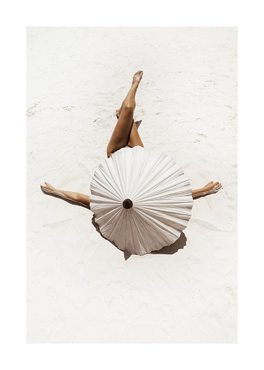  – Fotografie einer Frau, bedeckt von einem beigen Sonnenschirm, die mit gekreuzten Beinen im weißen Sand liegt