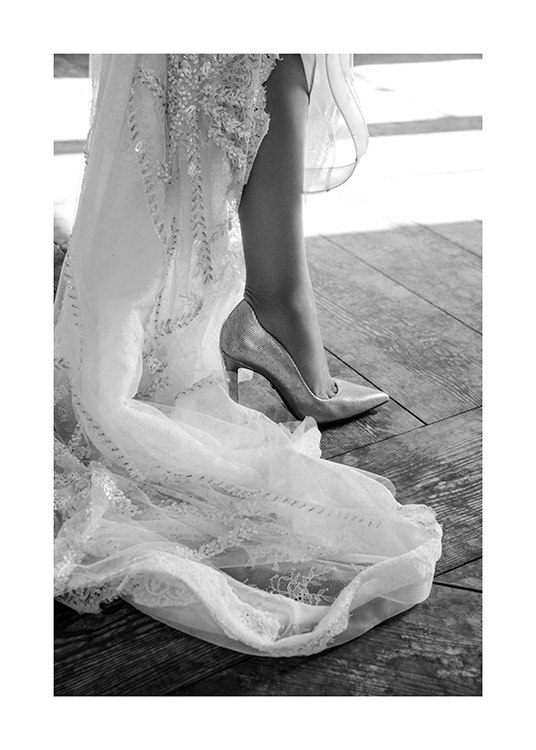  – Schwarz-weiß-Fotografie, das den Saum eines weißen Kleides mit Stickerei und einem High-Heel zeigt