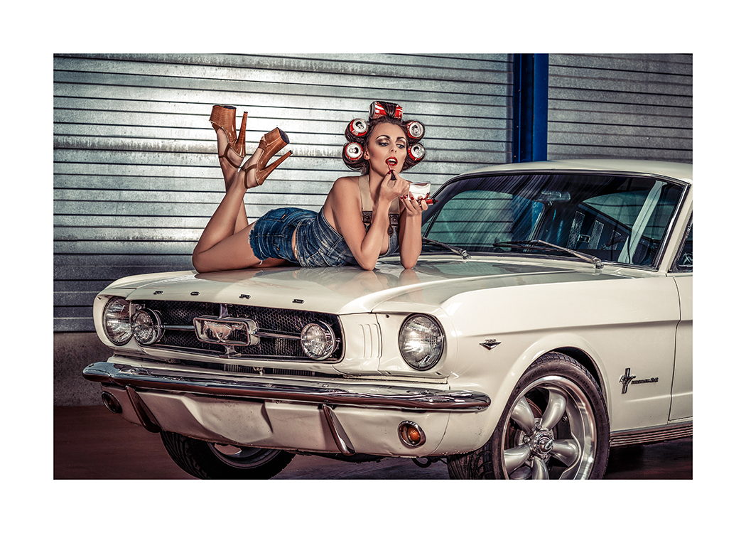  – Fotografie einer Frau, die auf der Kühlerhaube eines Autos liegt und Lippenstift aufträgt, im Haar trägt sie Getränkedosen