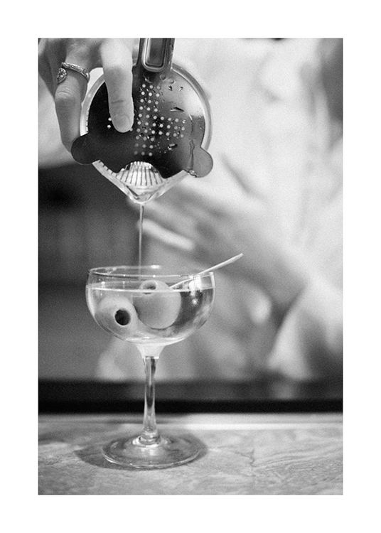  – Schwarz-weiß-Fotografie eines Martinis, der aus einem Cocktail-Shaker eingegossen wird, im Glas Oliven