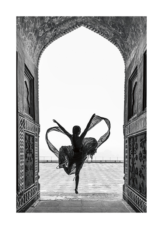  – Schwarz-weiß-Fotografie einer Frau, die in einem fließenden Kleid auf einem Bein tanzt, eingerahmt von einem Bogen