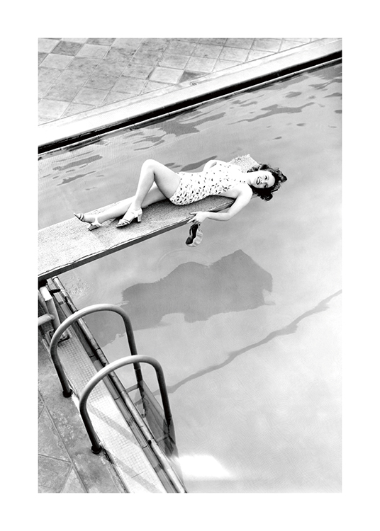  – Schwarz-weiß-Fotografie einer Frau, die auf einem Sprungbrett liegt, unter ihr ein Pool
