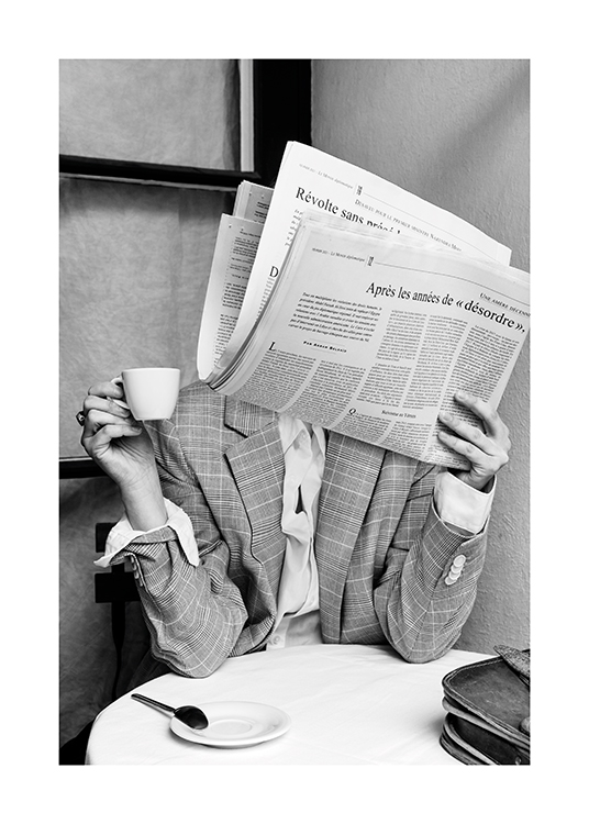  – Schwarz-weiß-Fotografie einer Person, die an einem Cafétisch sitzt und das Gesicht mit einer Zeitung verdeckt