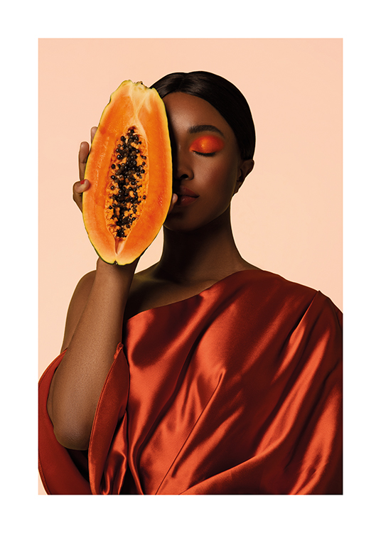  – Frau in Satinkleid, die eine geschnittene Papaya an ihr Gesicht hält