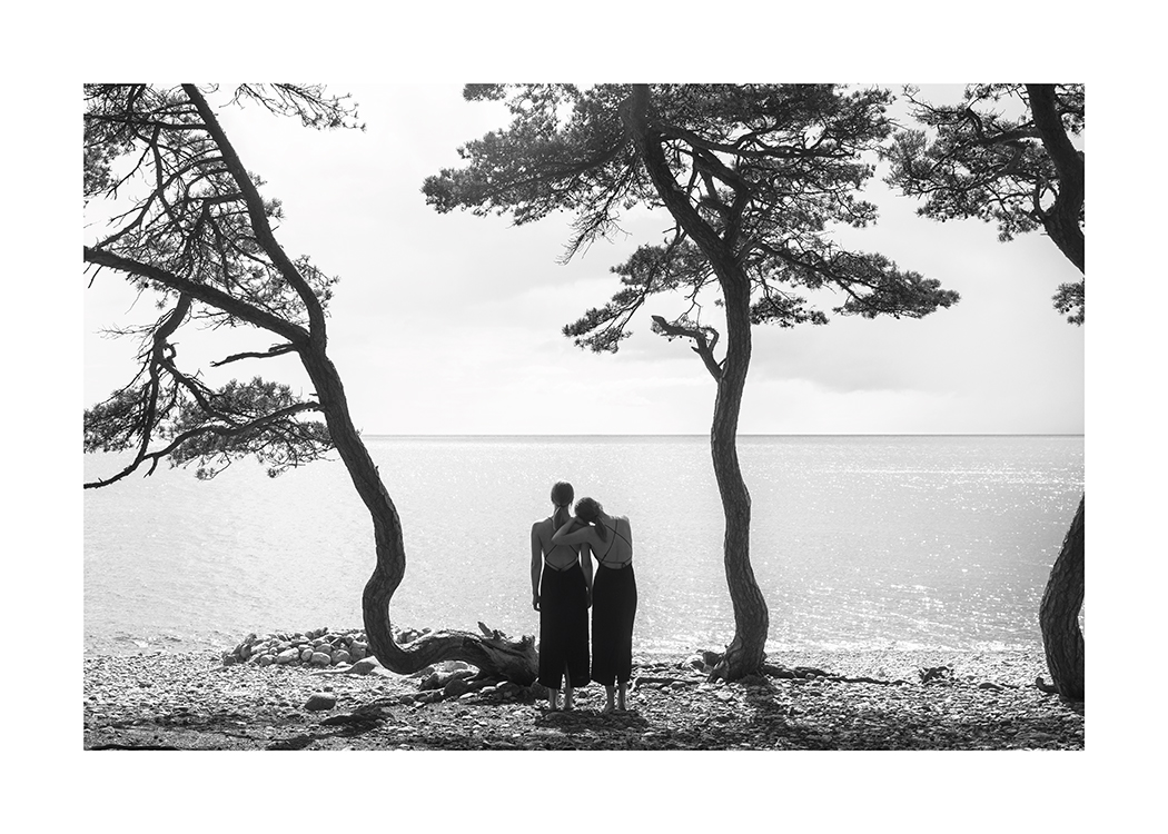  – Schwarz-weiß-Fotografie eines Frauenpaares, das von einem Strand mit Bäumen auf das Wasser schaut