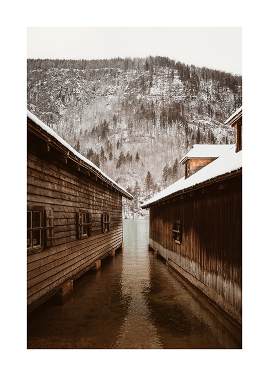  – Fotografie von zwei Bootshäusern vor einem Berg mit verschneitem Wald