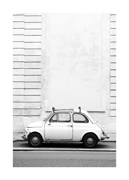  – Schwarz-Weiß-Fotografie eines kleinen Auto-Klassikers, der vor einer Gebäudefassade mit Streifeneffekt geparkt ist
