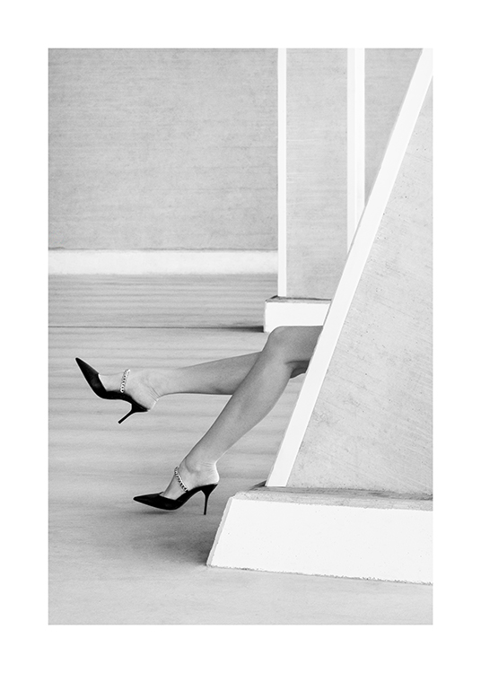– Schwarz-weiß-Fotografie eines Beinpaares mit High Heels, das hinter einer Wand hervorragt
